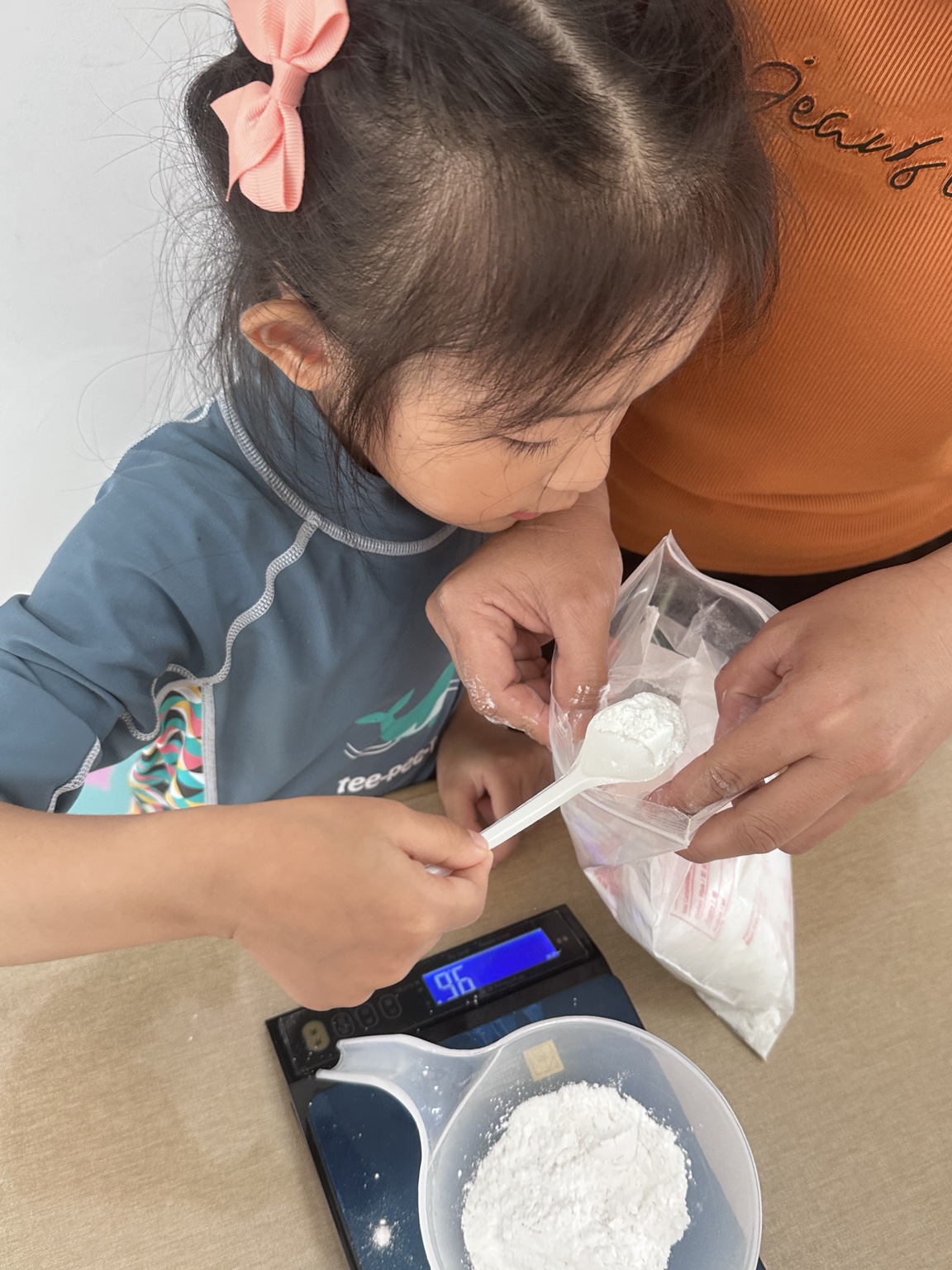 A child measuring an ingredient with an adult’s guidance