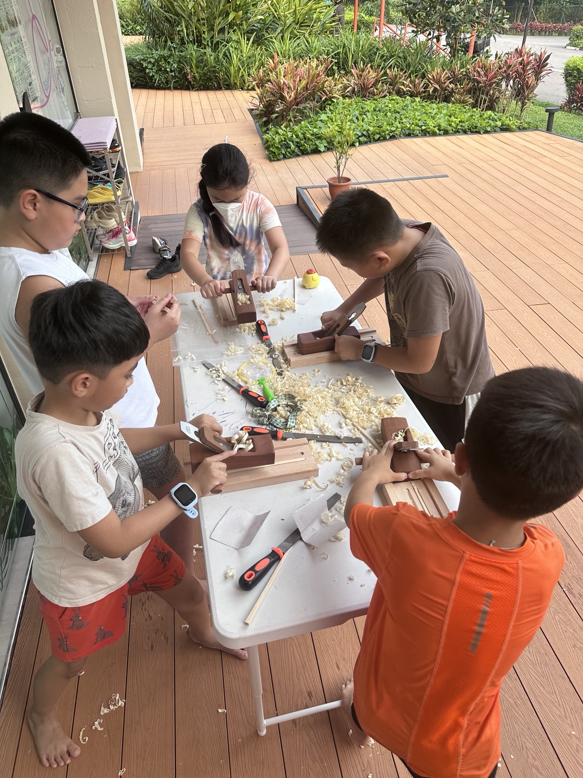 Children exploring wood planing around an outdoor workshop table